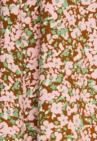 Un tissu fluide présentant un fond marron avec un motif éparpillé de fleurs roses et vertes, mettant en avant une texture douce et des couleurs vibrantes.