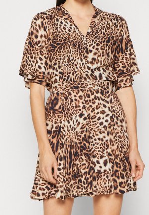 Femme portant une robe à manches courtes imprimée léopard, avec un col en V, une taille ajustée et une jupe évasée sur fond uni.