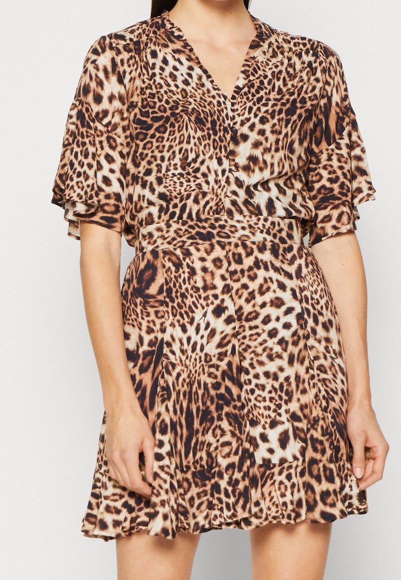 Femme portant une robe à manches courtes imprimée léopard, avec un col en V, une taille ajustée et une jupe évasée sur fond uni.