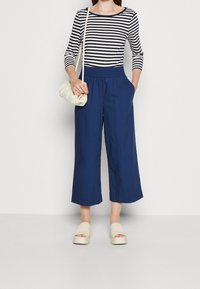 Navy brede culottes met een elastische tailleband, gecombineerd met een gestreepte lange mouwen top. Witte oversized tas en beige plateau sandalen.
