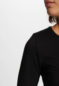 Maglietta nera a maniche lunghe con un design aderente, texture liscia e scollatura rotonda. Il tessuto sembra morbido e elastico.