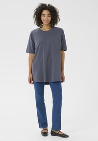 T-shirt grigia casual, a maniche corte, con scollo tondo e dietro più lunga, abbinato a jeans blu dritti e ballerine nere.