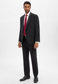 Abito nero con giacca monopetto, camicia bianca e cravatta rossa. Pantaloni neri e scarpe formali nere. Tessuto liscio e modello sartoriale.