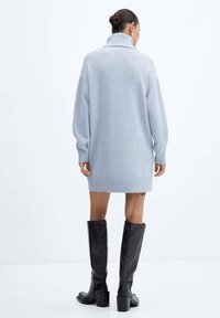 Robe-pull bleu clair oversize avec un col montant et un ourlet côtelé, associée à des bottes noires montantes à talon bloc.