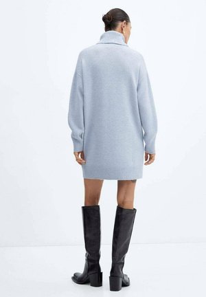 Robe-pull bleu clair oversize avec un col montant et un ourlet côtelé, associée à des bottes noires montantes à talon bloc.