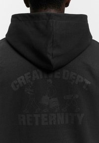 Black hooded sweatshirt with a matte texture. Features "CREATIVE DEPT." and "RETERNITY" in bold lettering above three walking figures.