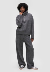 Sweter w kolorze węgla o wysokim kołnierzu i detalu z zamkiem, zestawiony z szerokimi spodniami w tym samym kolorze wykonanymi z miękkiego, teksturowanego materiału.