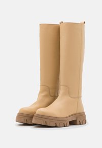 Kožené čižmy b�éžovej farby po kolená s masívnou gumovou podrážkou, zaoblenými špičkami a minimálnymi detailmi šitia. Obsahujú pútka pre jednoduché obúvanie.
