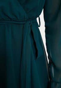 Robe enveloppante en teal en tissu léger et transparent, dotée d'une ceinture nouée à la taille et de manches évasées pour une silhouette fluide.