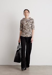 Leopard-print top with a boat neckline and three-quarter sleeves paired with black, wide-leg trousers and a black tote bag.