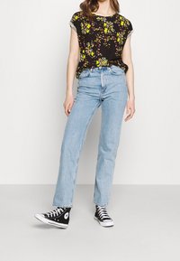 Czarny kwiatowy top z krótkim rękawem z żółtymi i białymi kwiatami, jasnoniebieskie dżinsy z wysokim stanem oraz czarne sneakersy za kostkę.