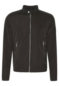 Svart lätt jacka med hög krage, dragkedja fram och två sidofickor med dragkedja. Har präglad logotypdetalj och slät textur.