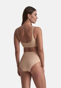 Donna che indossa un reggiseno beige senza cuciture e slip a vita alta, vista da dietro su uno sfondo chiaro e semplice.