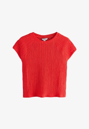 Crvena majica kratkih rukava izrađena od teksturiranog materijala s rebrastim uzorkom. Ima okrugli izrez i opušten, kutni kroj.