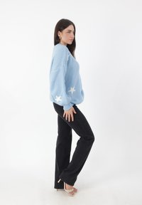 Lichtblauwe gebreide trui met witte sterrenpatronen, gecombineerd met zwarte flare jeans en beige hoge hakken. Textuurstof en relaxed fit.