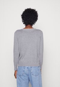 Harmaa neulepusero leveällä kauluksessa, ribbikuvioidut hihansuut ja helma, jossa on yksinkertainen, koristamaton muotoilu. Yhdistetty vaaleansinisiin farkkuihin.