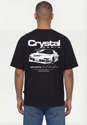 Mann von hinten gesehen, trägt ein schwarzes T-Shirt mit weißem Grafikmotiv eines Sportwagens und dem Text „Crystal Paris, No Limits, Just Motion.“