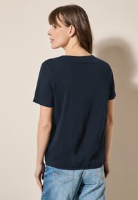Navyblå bomullströja med korta ärmar, rund halsringning och en avslappnad passform, kombinerad med ljustvättade jeans. Slät textur, minimal detaljering.