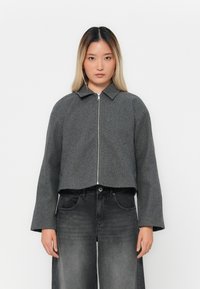 Giacca grigia corta realizzata in misto lana, con chiusura frontale a zip, maniche larghe e colletto classico. Abbinata a jeans grigio scuro.