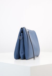 Modrá kožená kabelka s texturovaným povrchem, obdélníkový tvar, horní zipové uzavření a boční úchytka.