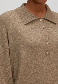 Beige gebreide sweater met een geribde kraag, voorzien van zes ronde knopen in een complementaire lichte tint, zachte textuur en een comfortabele pasvorm.