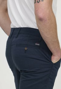 Chinos bleu marine en tissu léger, dotés d'une poche arrière avec une fermeture à bouton et d'une petite étiquette sur la ceinture.