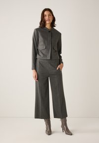 Graues, strukturiertes zweiteiliges Outfit mit einer gekürzten, knöpfbaren Jacke mit zwei Fronttaschen und weit geschnittenen Hosen, kombiniert mit grauen Stiefeletten.