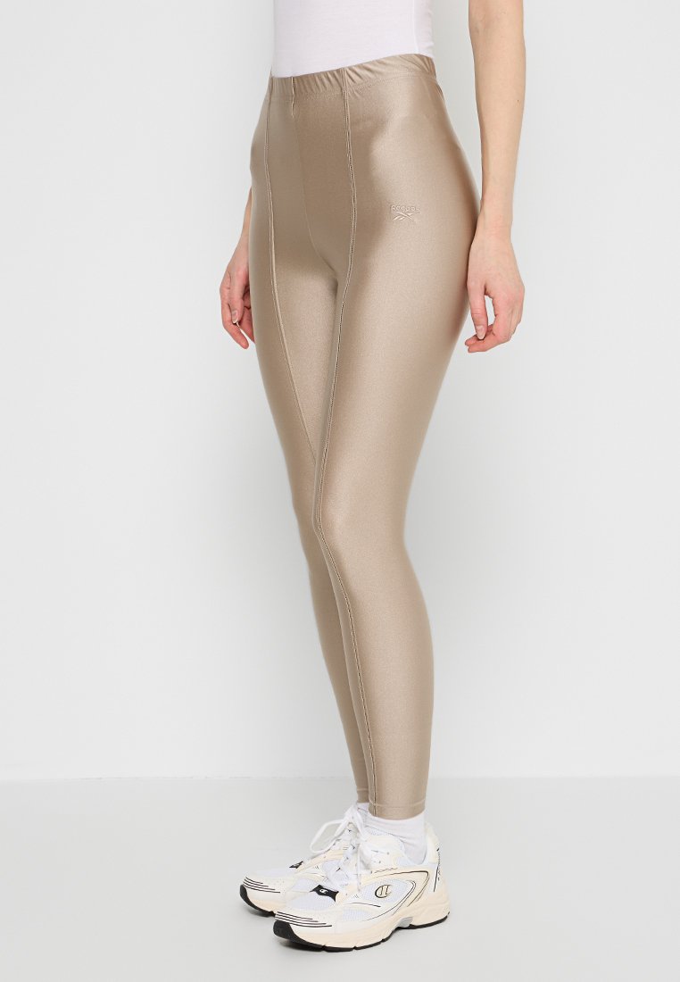 Beżowe legginsy z wysokim stanem o błyszczącej, gładkiej fakturze, dobrze dopasowane, z kontrastowym szwem po bokach.