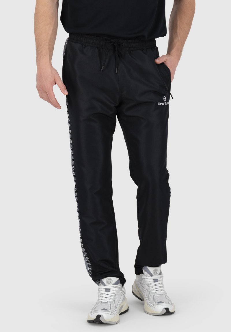Schwarze Sporthosen aus glattem Material mit einem Kordelzugbund, seitlichen Taschen und Logoakzenten entlang der Seitenstreifen.