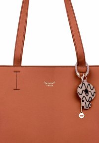 Hnědá kožená kabelka s prošíváním, s zlatým logem a ozdobným klíčenkou s vzorovaným kulatým přívěskem.