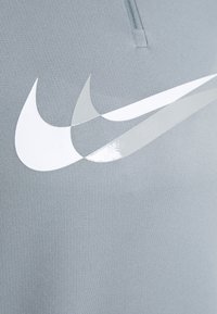Tessuto atletico grigio con un grande logo Nike bianco dall'aspetto lucido, su una superficie liscia e texturizzata.