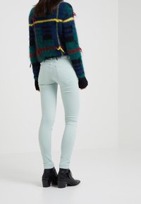 Fuzzy groen geruit sweater met gele en zwarte accenten, gecombineerd met lichtblauwe skinny jeans en zwarte enkellaarsjes.