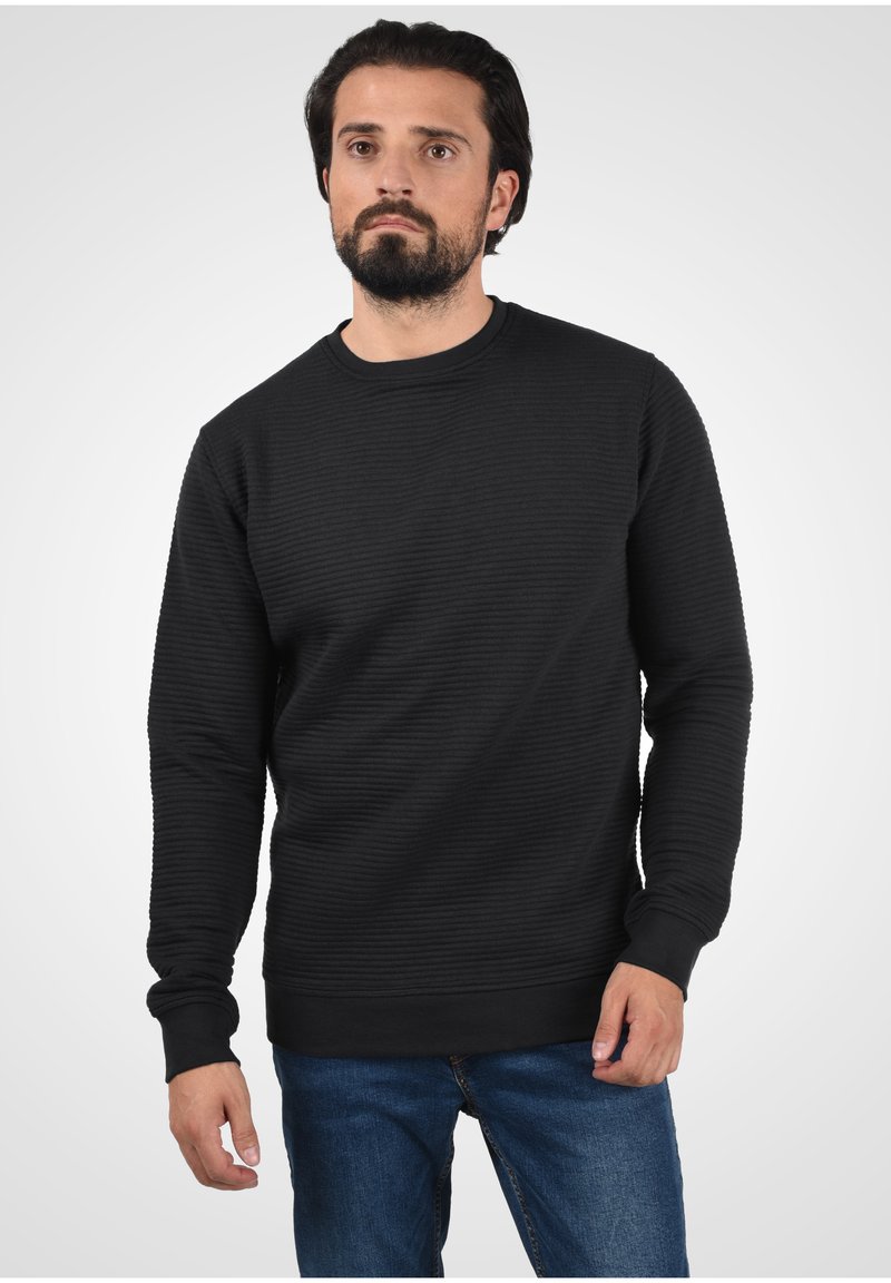 Musthave mustribaline sweatshirt pikad varrukad, ümar kaelus ja tekstuuriga kangas. Kombineeritud siniste teksadega, luues üleüldiselt sundimatu ilme.