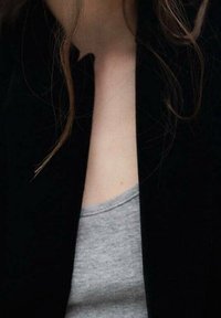 Col de veste noire avec un débardeur gris visible en dessous ; texture de tissu lisse ; léger éclat sur la veste.