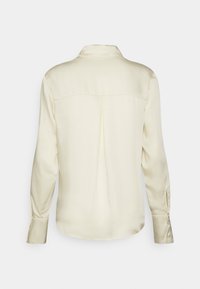 Kremfärgad satinblus med långa ärmar, krage och plisserad detalj på baksidan, med knappade manschetter och en slät textur.