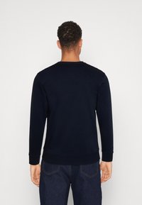 Sudadera de color azul marino con mangas largas, cuello redondo y puños acanalados. Textura suave con un corte relajado, combinada con jeans oscuros.