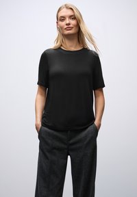 Zwarte korte mouwen top met een ronde halslijn, een gladde textuur en een relaxte pasvorm, gecombineerd met gestructureerde grijze wijde broek.