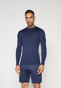 Rash guard azul-marinho de manga longa com costuras planas, gola alta e pequeno logótipo no ombro, combinado com calções azul-marinho a condizer.