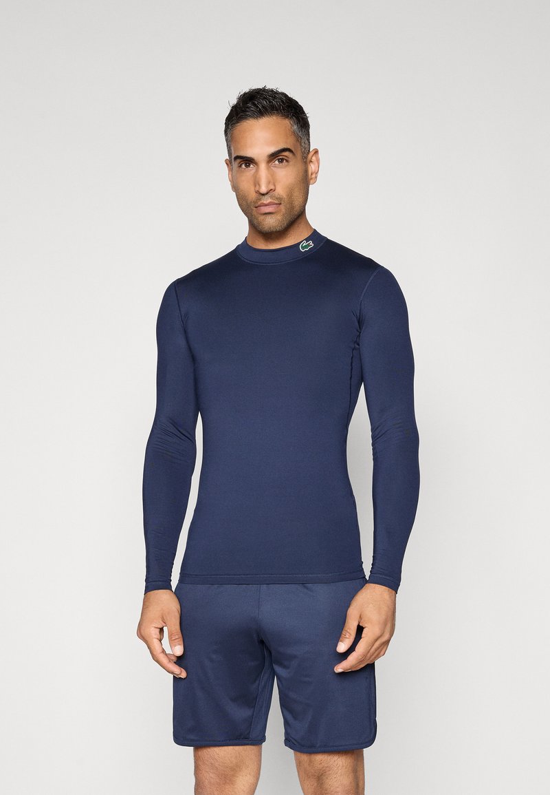 Rash guard azul-marinho de manga longa com costuras planas, gola alta e pequeno logótipo no ombro, combinado com calções azul-marinho a condizer.