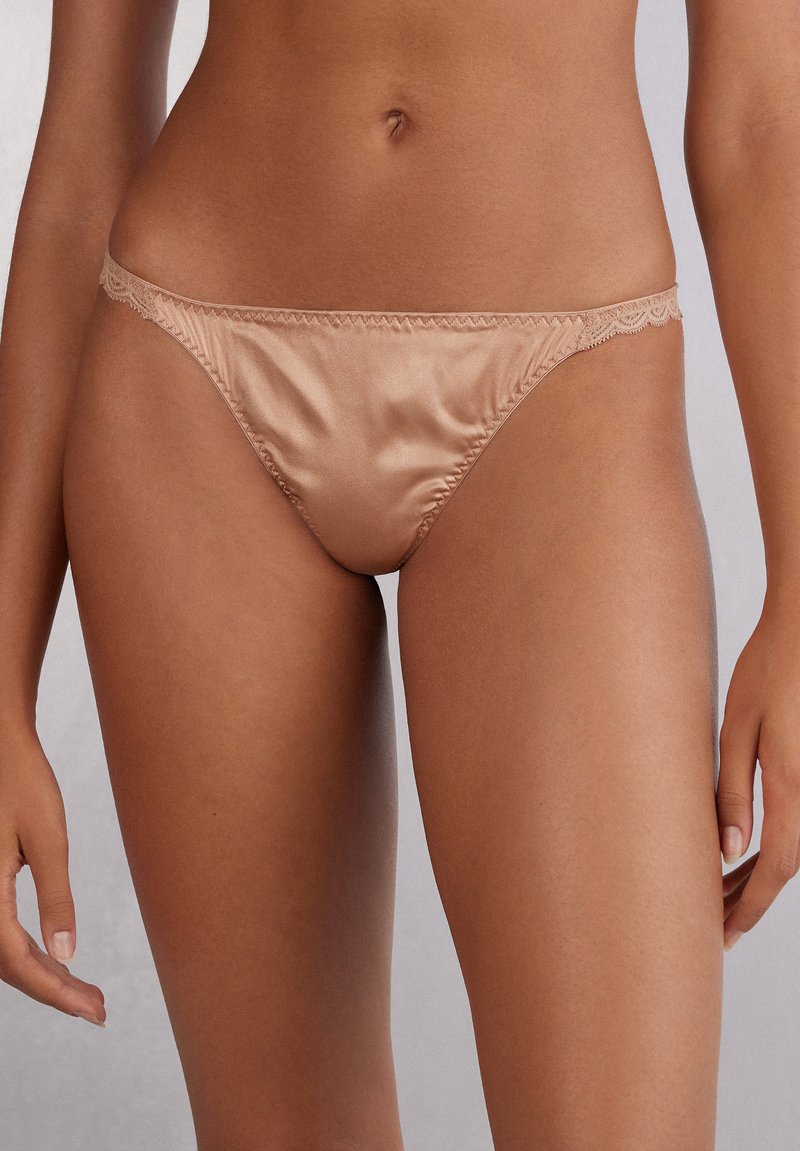 Satinstringtrosor i en varm beige nyans med delikat spetsdetalj längs midjan, med en mjuk yta och minimal täckning.
