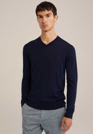 V-neck sweater in dark navy, lightweight knit material, long sleeves, ribbed cuffs and hem, paired with light gray patterned trousers.