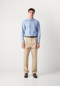 Camisa azul clara de botão com mangas longas, calças creme e sapatos castanhos escuros, usados com um cinto preto. Texturas de tecido suave.