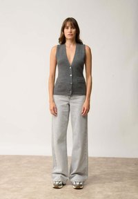 Top sin mangas gris con un profundo escote en V y cierre frontal de botones, combinado con jeans de pierna ancha de un gris claro y zapatillas con estampado.