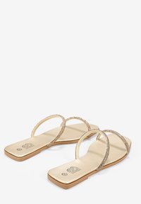 Sandalias de oro con suelas planas, que cuentan con dos cintas cruzadas brillantes, textura suave y un diseño simple y minimalista.