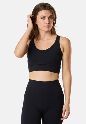 Black athletic crop top with a scoop neckline and wide straps, made from a smooth, stretchy fabric. Worn with high-waisted black leggings.