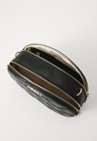 Borsa in pelle trapuntata nera con zip dorate e un interno chiaro. Presenta due scomparti con una texture liscia e forma rotonda.