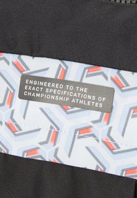 Black fabric with a textured finish, featuring a light blue patterned strip showcasing geometric designs in gray and red. Includes a gray label with white text.