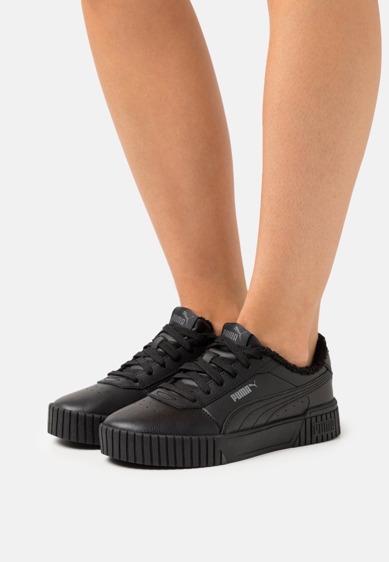 Baskets noires avec une tige en cuir texturé, une semelle en caoutchouc texturée et une bordure en peluche le long du col. Elles présentent un design à lacets et un branding discret.