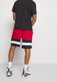 Rode sportieve shorts met zwart-witte horizontale strepen, gecombineerd met een zwart T-shirt en witte sneakers. Eenvoudig ontwerp, lichtgewicht stof.