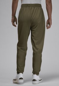Olivengrønne joggingbukser med elastisk talje og tætsiddende benmanchetter, parret med hvide sneakers med sorte accenter.